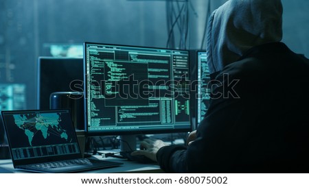 Dangerous Hooded Hacker Breaks into Government Data Servers and Infects Their System with a Virus. His Hideout Place has Dark Atmosphere, Multiple Displays, Cables Everywhere.