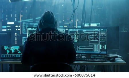 Dangerous Hooded Hacker Breaks into Government Data Servers and Infects Their System with a Virus. His Hideout Place has Dark Atmosphere, Multiple Displays, Cables Everywhere.
