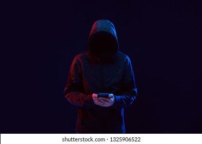 Dangerous hooded hacker. Internet, cyber crime, cyber attack, system breaking and malware concept. Dark face. Anonymous holding smartphone in hands.
