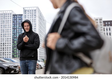 Dangerous man is calling little child girl on city street, kidnapping. copy space. criminal guy in black wear commit crime, ask girl to came to him. focus on guy. caucasian child in leather jacket