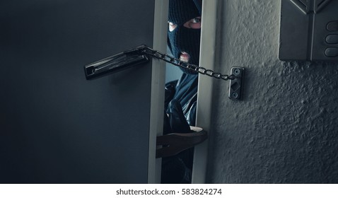 dangerous masked burglar with crowbar breaking into a victim's home door