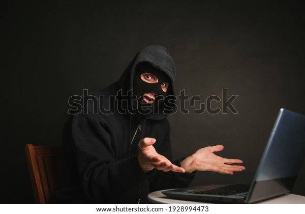 A\
dangerous masked hacker with a hood cannot infiltrate the data\
servers and infect them with viruses. Caught the criminal through a\
laptop. Photo on a dark background in the\
studio