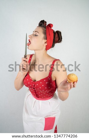 dangerous pin up girl housewife in red vintage polka dot dress stands with a huge kitchen knife in her hands and angrily rejoices on white solid studio background