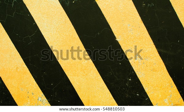 Dangerous road sign. Black and yellow stripes on\
concrete block texture. Dangerous way concept. Serpentine roadside\
stop. Danger on highway. Safe drive reminder. Yellow black paint on\
rough texture