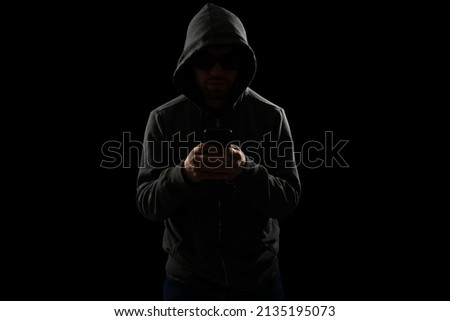 Dangerous scammer with a hoodie texting on the smartphone and committing online fraud