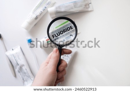 Dangerous toothpaste ingredient fluoride. Checking the composition of toothpaste with a magnifying glass against the background of many tubes