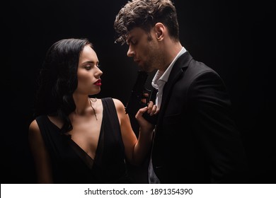 dangerous woman holding gun near man in suit isolated on black