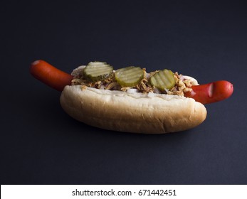 Danish hot dog with red sausage, ketchup, mustard sauce, raw and fried onions and pickled cucumbers isolated on black background