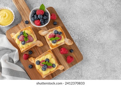 Danish puff pastry cakes with custard cream and fresh berries, sprinkled with powdered sugar on a wooden board on a concrete background. Top view, copy space - Powered by Shutterstock