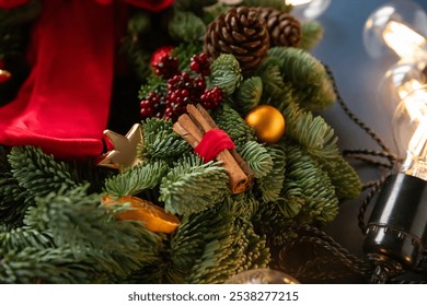 Danish spruce wreath. A beautifully arranged Christmas wreath features fragrant cinnamon sticks, pinecones, and colorful ornaments, illuminated by soft, warm lights. Wreath detail - Powered by Shutterstock