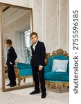 A dapper young boy, wearing a smart navy suit and tie, stands indoors in a grand room during the day.