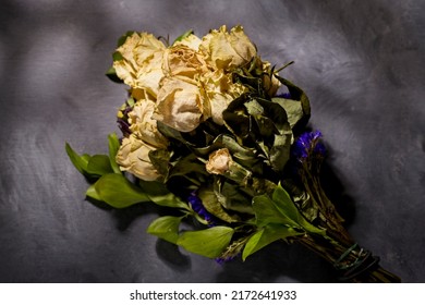 A Dappled Light Studio Photo Of A Bouquet Of Dried Yellow Roses On A Table.