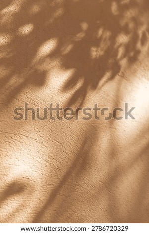Dappled sunlight through leaves creates a soft pattern on an ochre plaster wall. Warm Mediterranean aesthetic, abstract nature background, tranquil atmosphere, summer travel vibes concept.