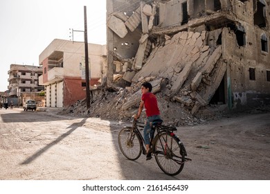 Darayya, Syria - April, 2022: Kid on bicycle on street in destroyed city after the Syrian Civil War.
