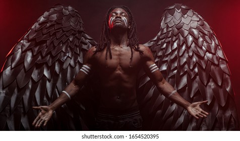 Dark African Angel With Big Black Wings Isolated, Young Serious Muscular Man Wearing Big Wings On The Back. Strong Angel Come Down From Heaven. Fantasy