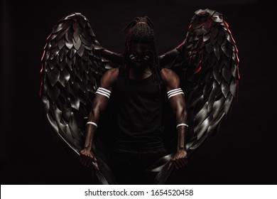 Dark African Angel With Big Black Wings Isolated, Young Serious Muscular Man Wearing Big Wings On The Back. Strong Angel Come Down From Heaven. Fantasy