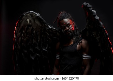 Dark African Angel With Big Black Wings Isolated, Young Serious Muscular Man Wearing Big Wings On The Back. Strong Angel Come Down From Heaven. Fantasy