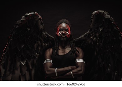 Dark African Angel With Big Black Wings Isolated, Young Serious Muscular Man Wearing Big Wings On The Back. Strong Angel Come Down From Heaven. Fantasy