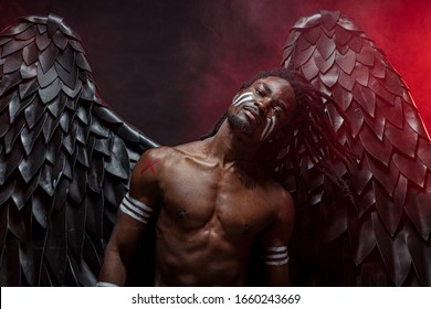 Dark African Angel With Big Black Wings Isolated, Young Serious Muscular Man Wearing Big Wings On The Back. Strong Angel Come Down From Heaven. Fantasy