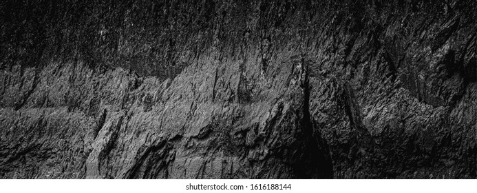 Dark Aged Shabby Cliff Face And Divided By Huge Cracks And Layers. Coarse, Rough Gray Stone Or Rock Texture Of Mountains, Wide And Panoramic Background For Text On Theme Geology And Mountaineering.