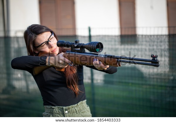 Dark air girl woman with protection glasses holding\
a air rifle diablo WEIHRAUCH HW 77 K SPRING shooting targets in a\
garden grass