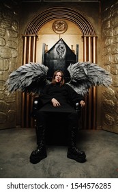 Dark Angel Man With Huge Wings In Black Outfit Sitting On The Throne On Golden Gates Background Alone