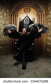 Dark Angel Man With Huge Wings In Black Outfit Sitting On The Throne On Golden Gates Background Alone