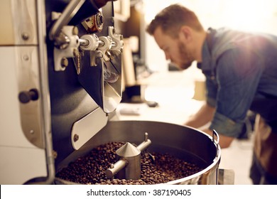 Dark and aromatic coffee beans in a modern roasting machine with the blurred image of the professional coffee roaster visible in the background