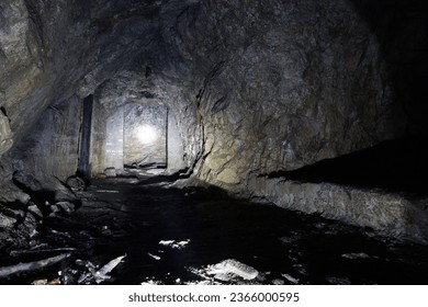 A dark artificial stone cave in the mountains. The light from the lantern falls on the rocks, where there are passages in the form of doors. Everything is wet. There are old branches and bricks.