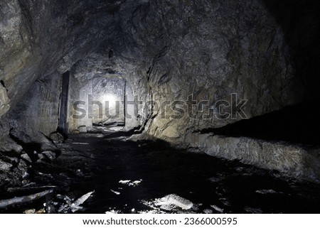 A dark artificial stone cave in the mountains. The light from the lantern falls on the rocks, where there are passages in the form of doors. Everything is wet. There are old branches and bricks.
