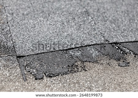 Dark asphalt patch applied to light gray roofing material. Worn patch of roof with visible signs of repair and aging, including rough textures and discolored areas