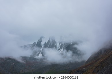 Dark Atmospheric Landscape With High Snow Mountains In Dense Fog In Rainy Weather. Large Snowy Mountain Range In Thick Fog In Dramatic Overcast. Snow-covered Rocky Mountains In Low Clouds During Rain.