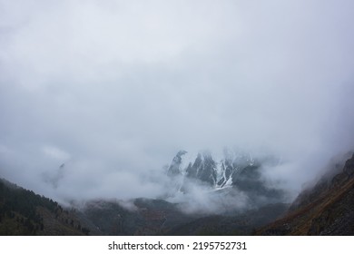 Dark Atmospheric Landscape With High Snow Mountains In Dense Fog In Rainy Weather. Large Snowy Mountain Range In Thick Fog In Dramatic Overcast. Snow-covered Rocky Mountains In Low Clouds During Rain.