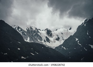 Dark atmospheric mountain landscape with glacier on black rocks in lead gray cloudy sky. Snowy mountains in gray low clouds in rainy weather. Gloomy mountain landscape with rocky mountains with snow. - Powered by Shutterstock