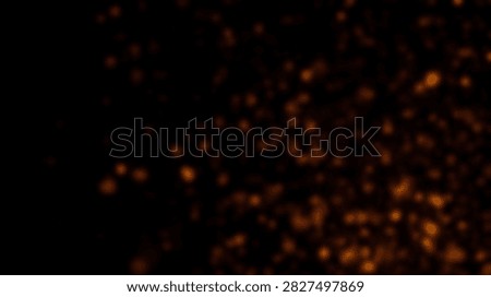 A dark background with many small, glowing particles of orange and yellow, creating an abstract effect.