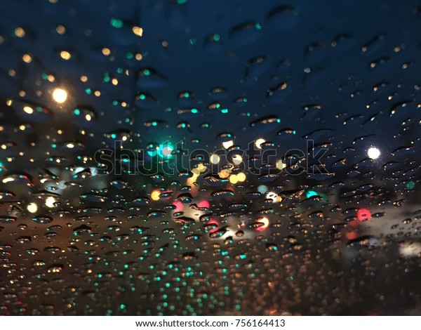 Dark background, raindrop on\
the windshield, street lights at night on a rainy day, colorful\
bokeh.