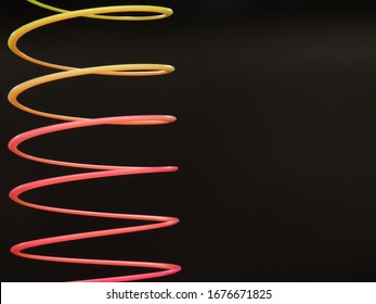 Dark background with yellow and pink slinky toy spiral one side frame. Isolated plastic toy in black background. Spring toy. Magic plastic toy. Spiral on black background. Copy space. Creative concept