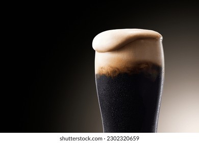 Dark beer, cold beer with bubbles overflowing from glass with water droplets