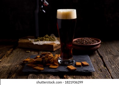 Dark Beer With Foam In A Glass. On A Dark Background Bottle And Ingredients For Beer, Malt, Hops. Home Brewery. Background Image