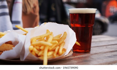 Dark Beer And Fries On A Wooden Table. Food Court. Takeaway Food, Food Festival. Unhealthy Food Concept. Focus On The Plastic Beer Glass