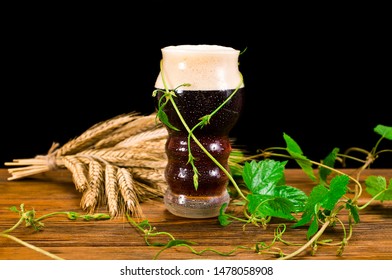 Dark beer with natural green hop leaves and dry wheat ears on a wooden background. Craft beer concept. 