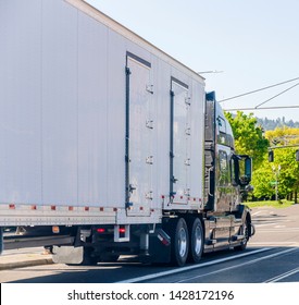 Dark Big Rig Long Haul Professional Comfortable Semi Truck Transporting Commercial Cargo In Covered Semi Trailer With Several Side Doors Driving On The City Street Going Through The Intersection