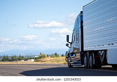 Dark Big Rig Modern Professional Popular Semi Truck Transporting Perishable Food In Chilled Refrigerated Semi Trailer Running On Divided Local Road With Meadow View And Clouds For Delivery Goods