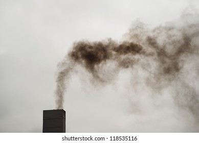 Dark Black Smoke From The Chimney On A Cold, Cloudy Day.