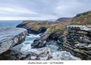 dark, black steep cliffs on the sea, where only the grass grows; blue-green sea with white waves on rocky shores; sea landscape with rocks and sea