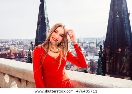 Dark blonde woman touches her hair while posing in red dress