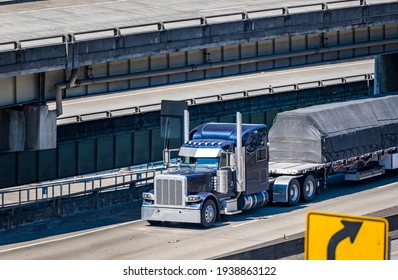 Dark Blue Classic Industrial Diesel Big Rig Semi Truck Tractor Transporting Covered Commercial Cargo On Flat Bed Semi Trailer Running On Multilevel Overpass Highway Road Intersection