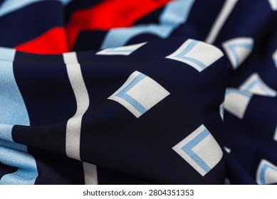 Dark blue fabric with geometric pattern in white, light blue and red colors. Folded textile in close-up view showing soft texture, draped cloth and modern decorative print.