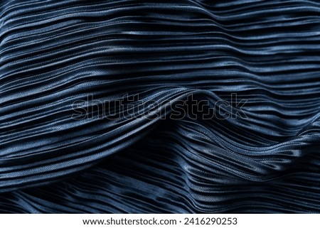 A dark blue pleated fabric with a shiny texture and intricate folds. It has an artistic feel due to the play of light and shadow on the folds