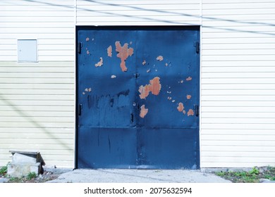 Dark Blue Vintage Garage Door With Peeling Rusty Paint. The Doors To The Garage Are Covered With Siding. Private Auto Repair Shop.